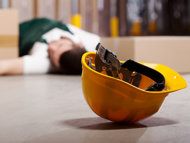 עובד שוכב על הרצפה אחרי תאונת עבודה וקסדת מגן צהובה